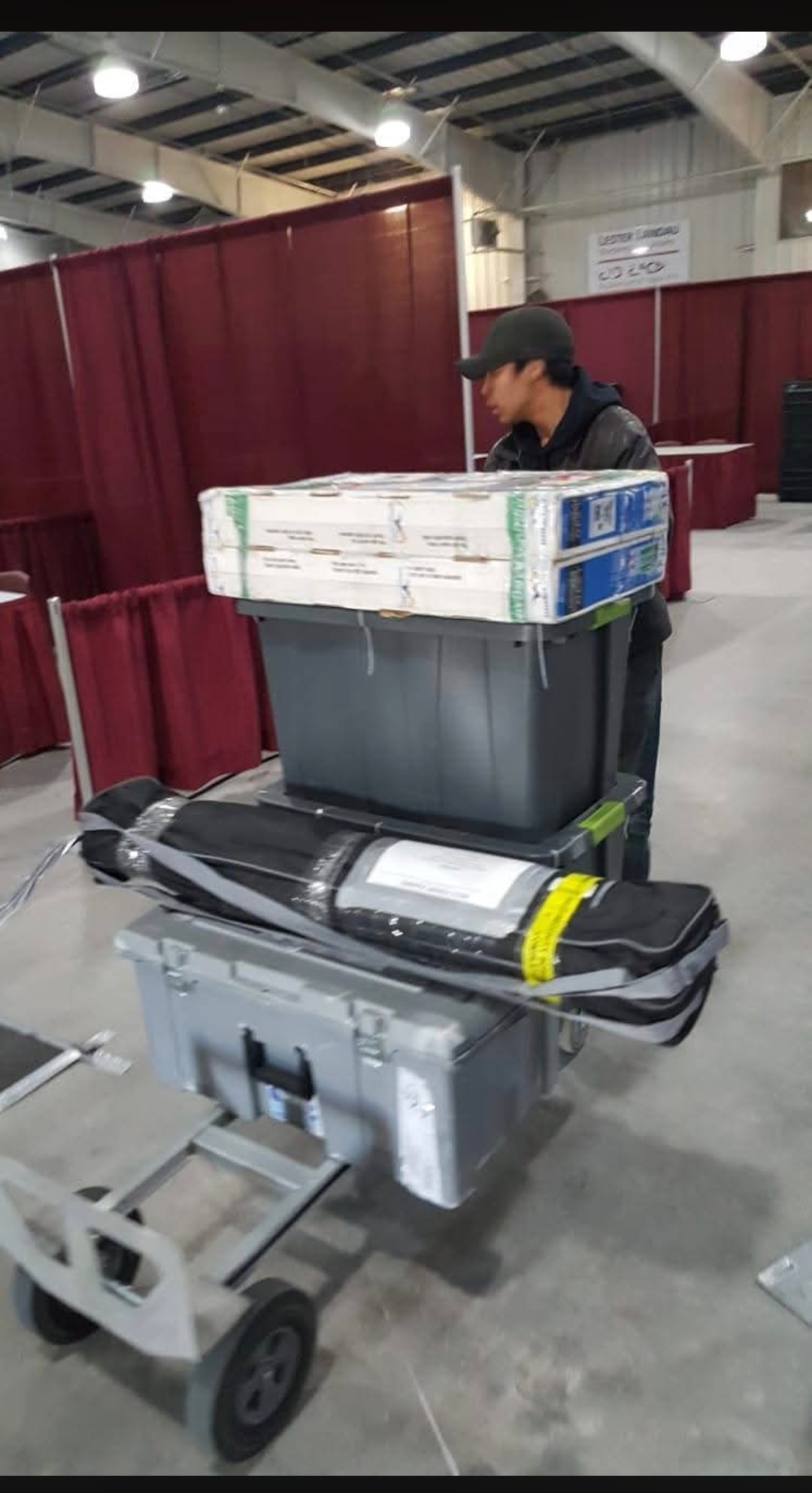 NMS team member moving stacked bins and cargo on a hand truck inside a venue