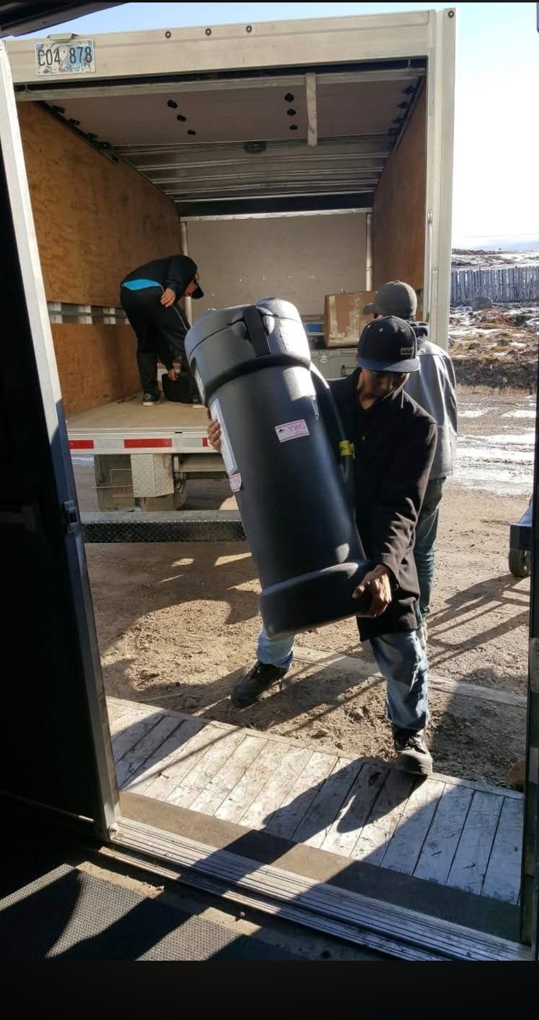 Two NMS movers loading a large cylindrical item into a moving truck outdoors in Nunavut